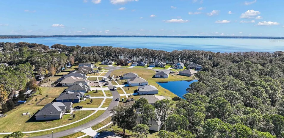 Aerial view of a serene neighborhood featuring homes surrounded by lush greenery and a shimmering body of water.