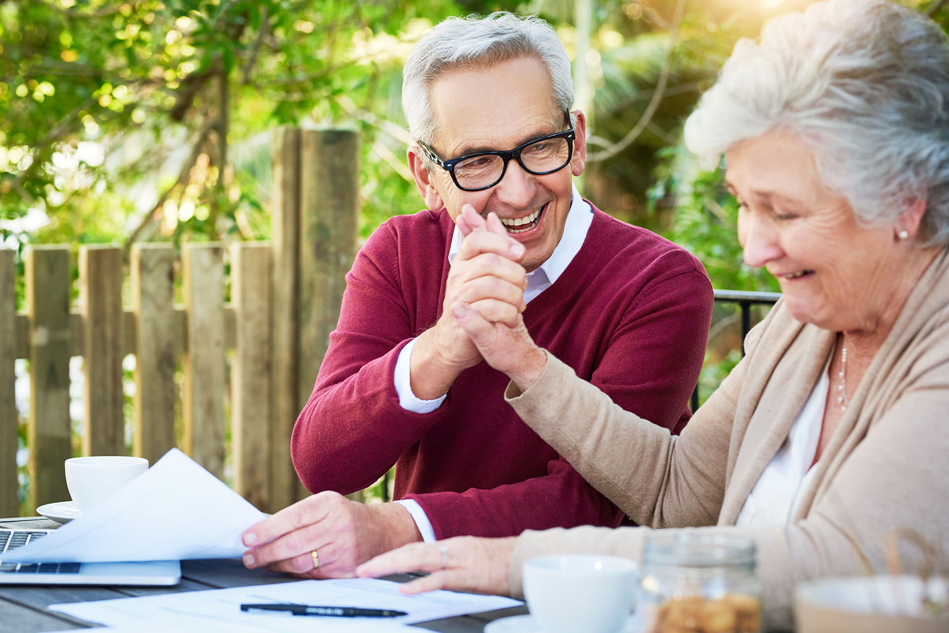 An older couple sits at a table, engaged with a laptop and papers, sharing ideas and collaborating on a project.