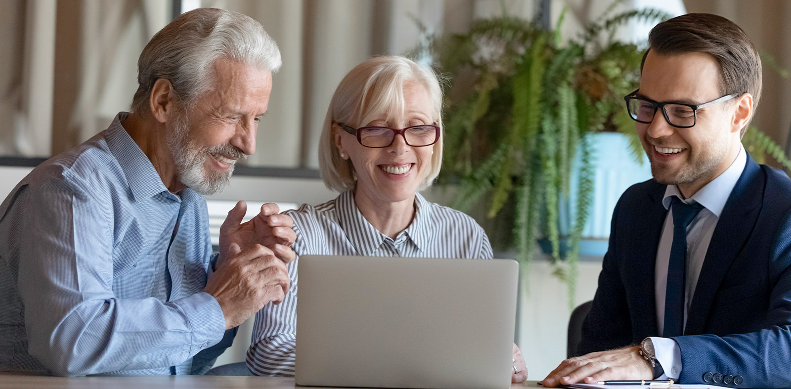 Three individuals seated at a table, focused on a laptop while discussing investment opportunities.