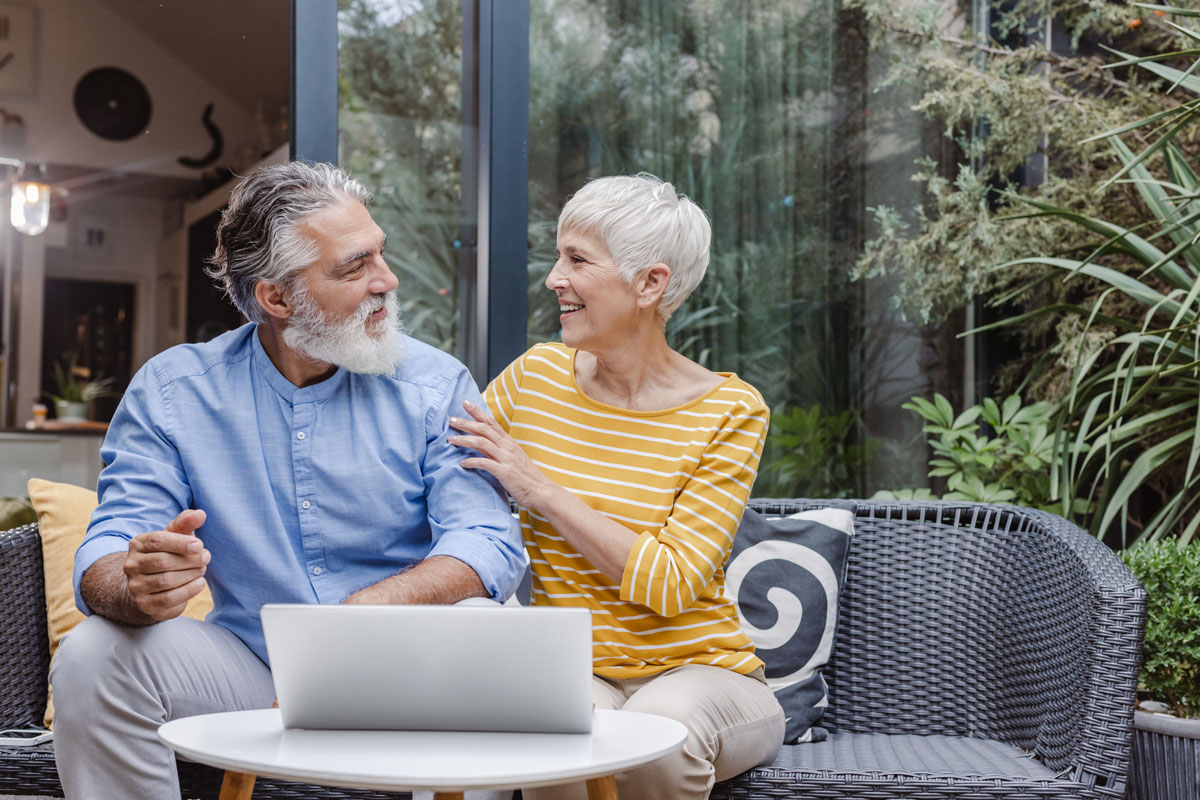A senior couple is at home on the balcony. They are spending time together and surfing the Net via laptop